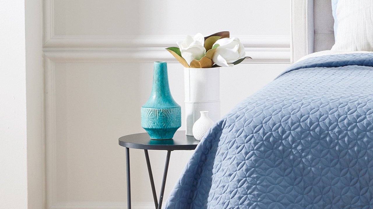 Decorative shot of bedside table, vases and flowers beside SlumberCorp bed.